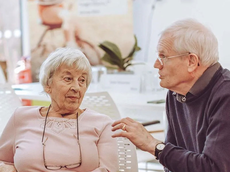 Man in mouave shirt sat explaining to quizzical women in pink blouse