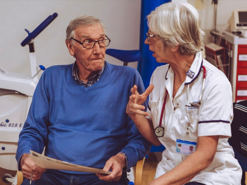 Older man in blue jumper chatting with nurse
