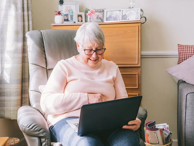 Woman in pink jumper happily using laptop